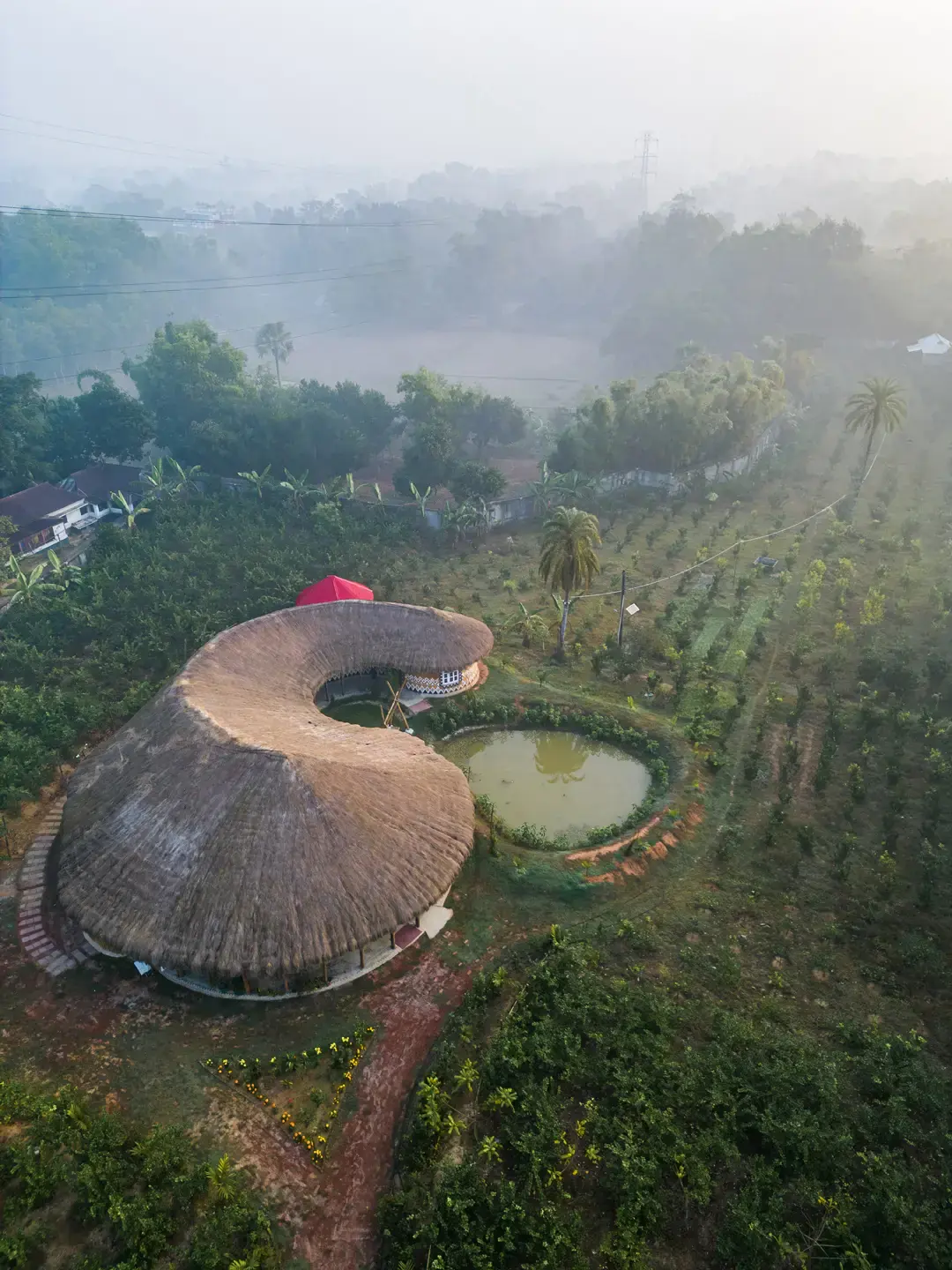Aerial view through morning mist of the curving thatched roof and ponds