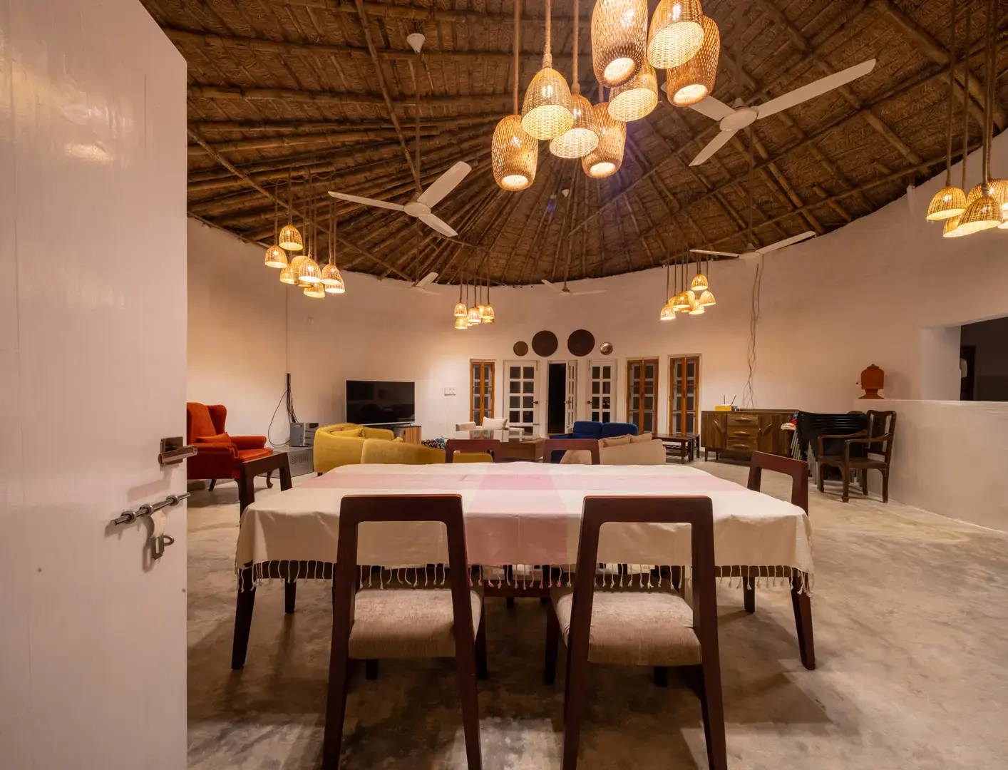Dining hall beneath a thatched ceiling with woven pendant lamps