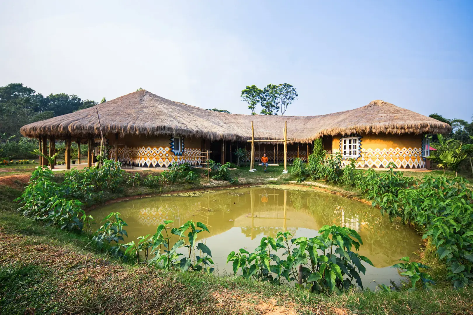 Thatched pavilions of the Eco Vacation House seen across the pond in daylight